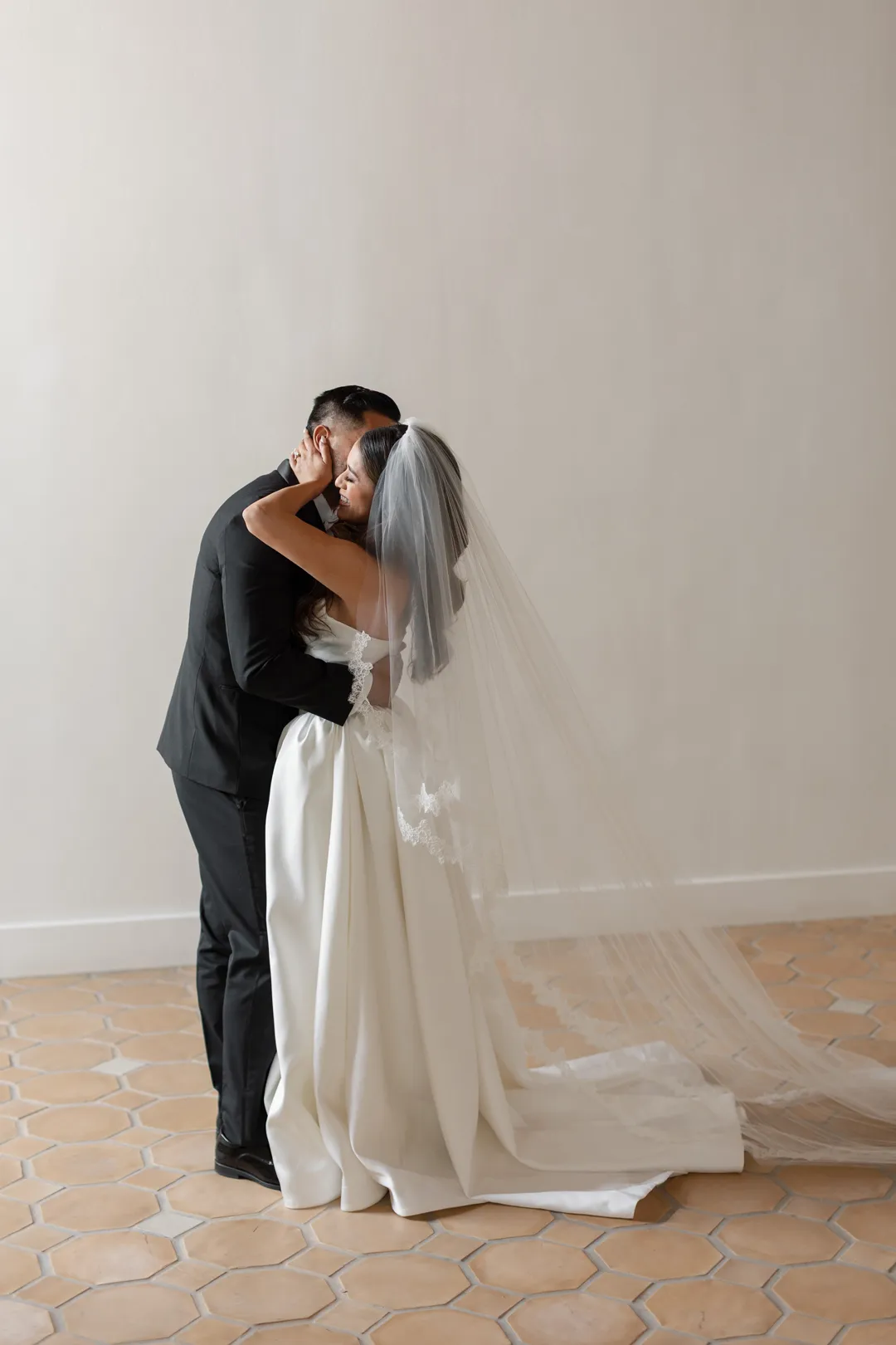 Wedding couple kissing beside a tall sunlit window.