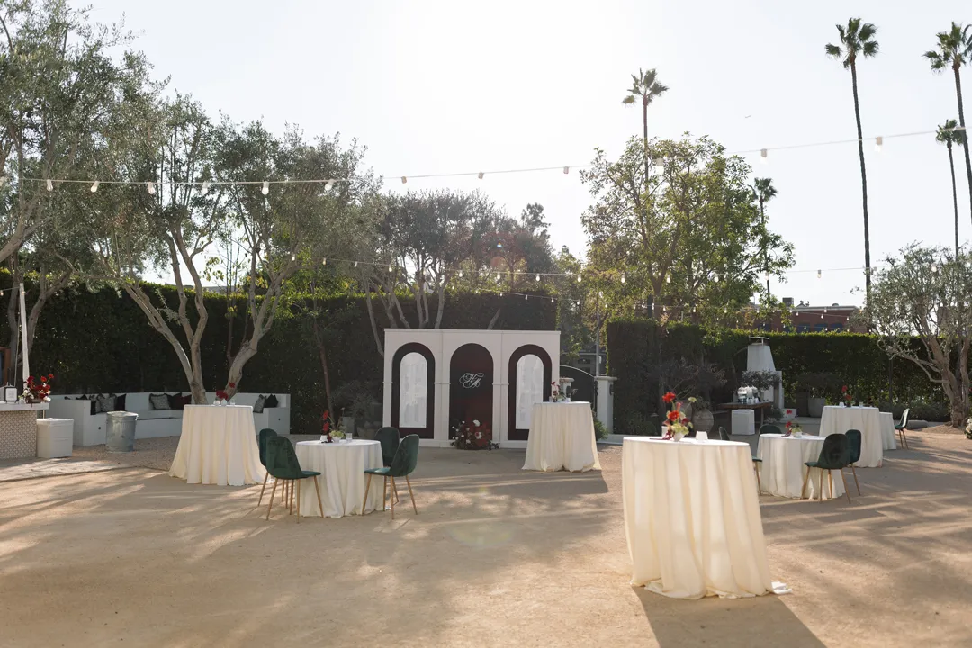 Courtyard cocktail-hour tables with green chairs beneath olive trees.