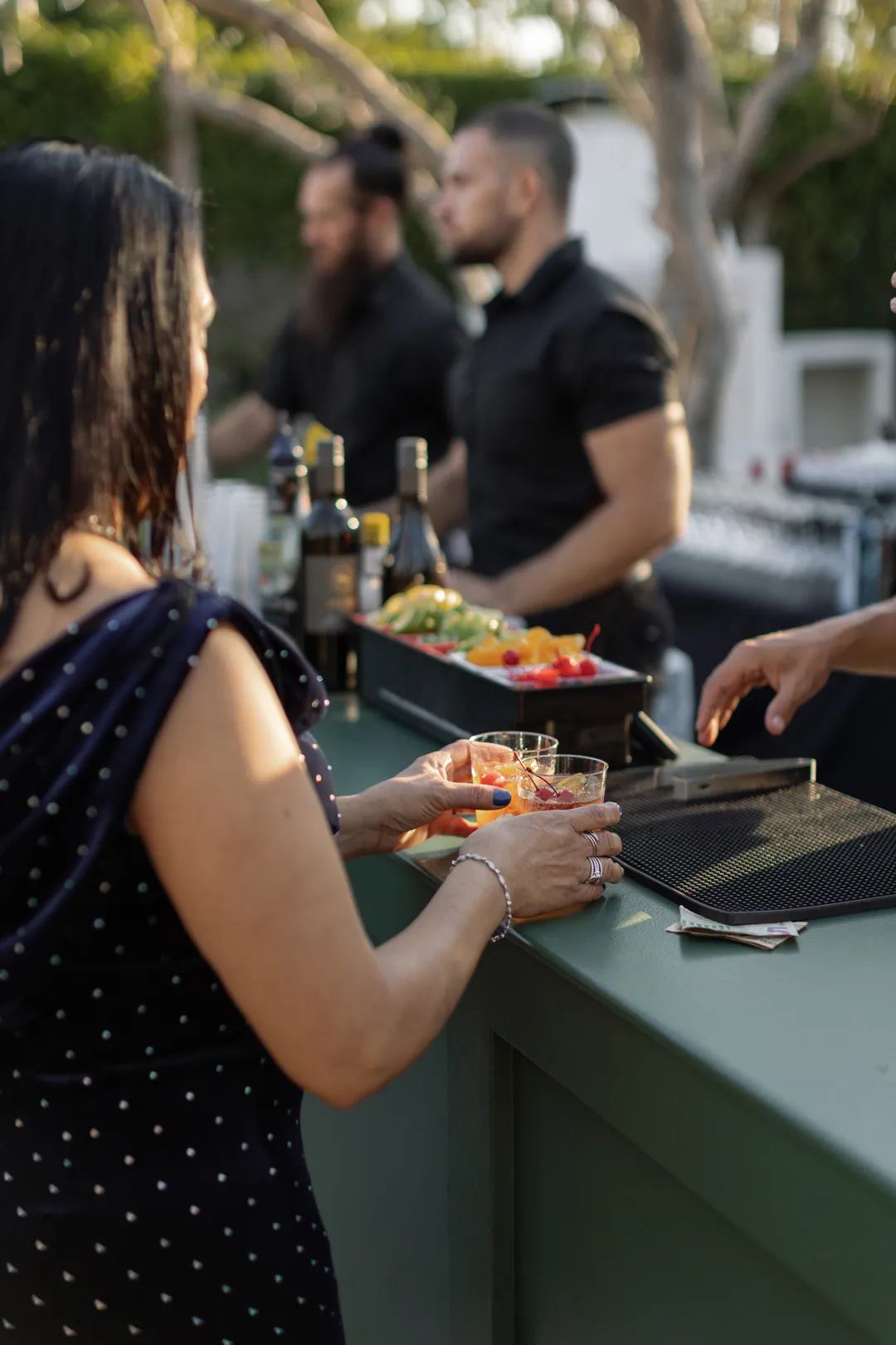 Bartenders serving cocktails to guests at the green outdoor bar.