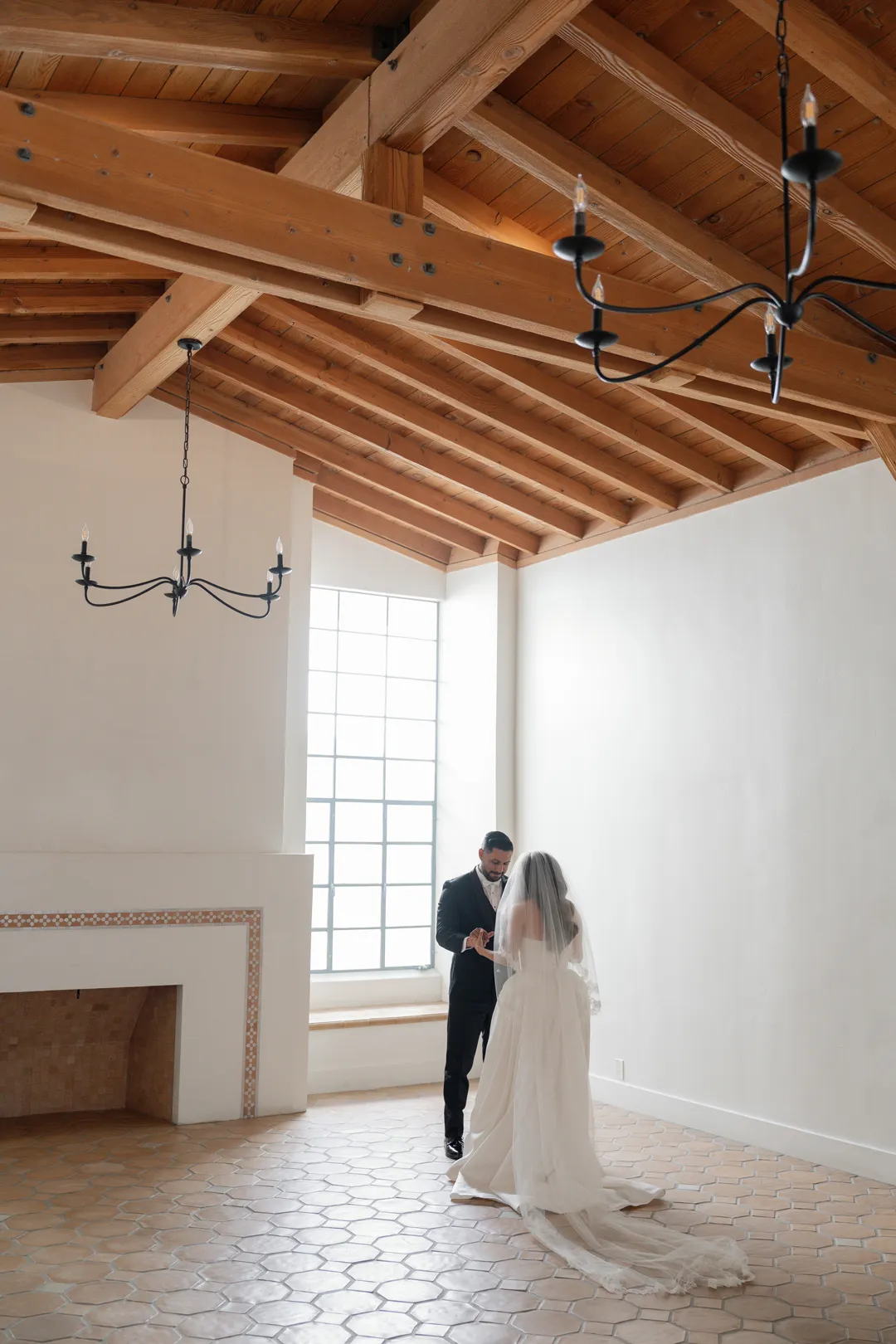 Wedding couple beneath exposed wooden beams in a sunlit room.