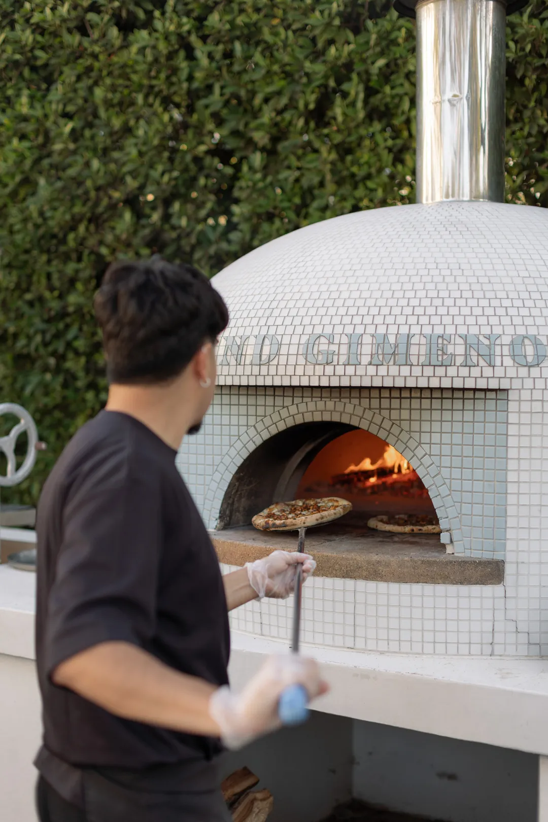 Catering team member tending a pizza in a wood-fired oven.