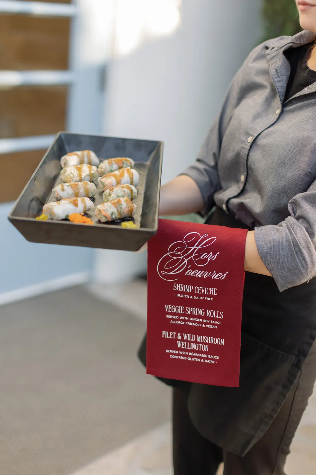 Server carrying a tray of spring rolls with a burgundy appetizer menu.