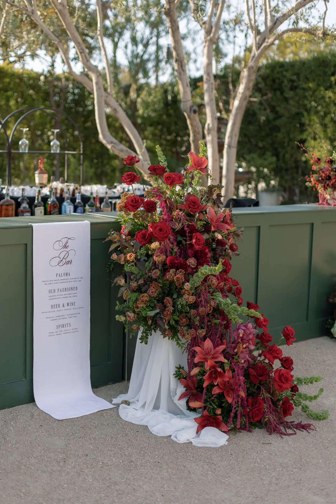Red floral arrangement cascading beside the green bar's cocktail menu.