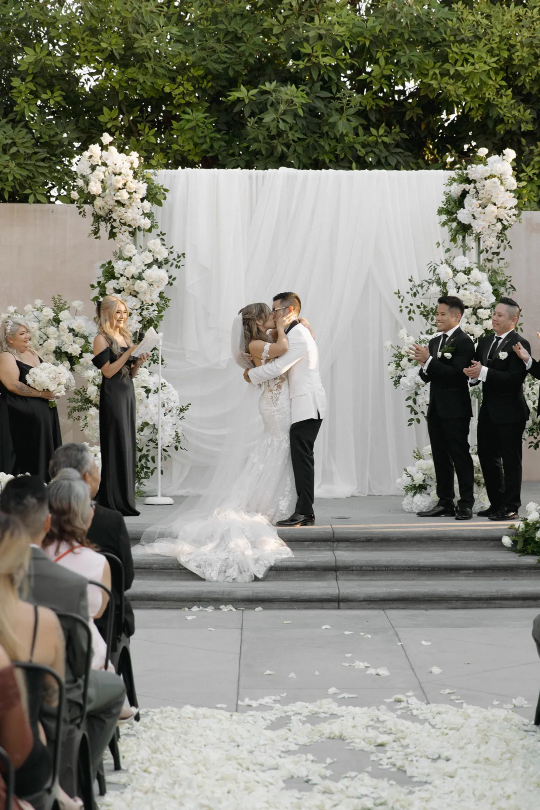 Wedding couple kissing as their wedding party applauds.