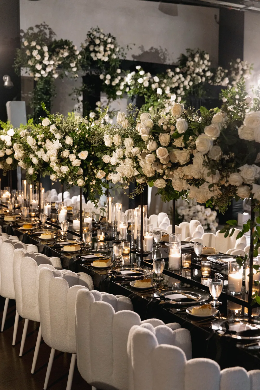 Long black reception table with white chairs and tall floral centerpieces.