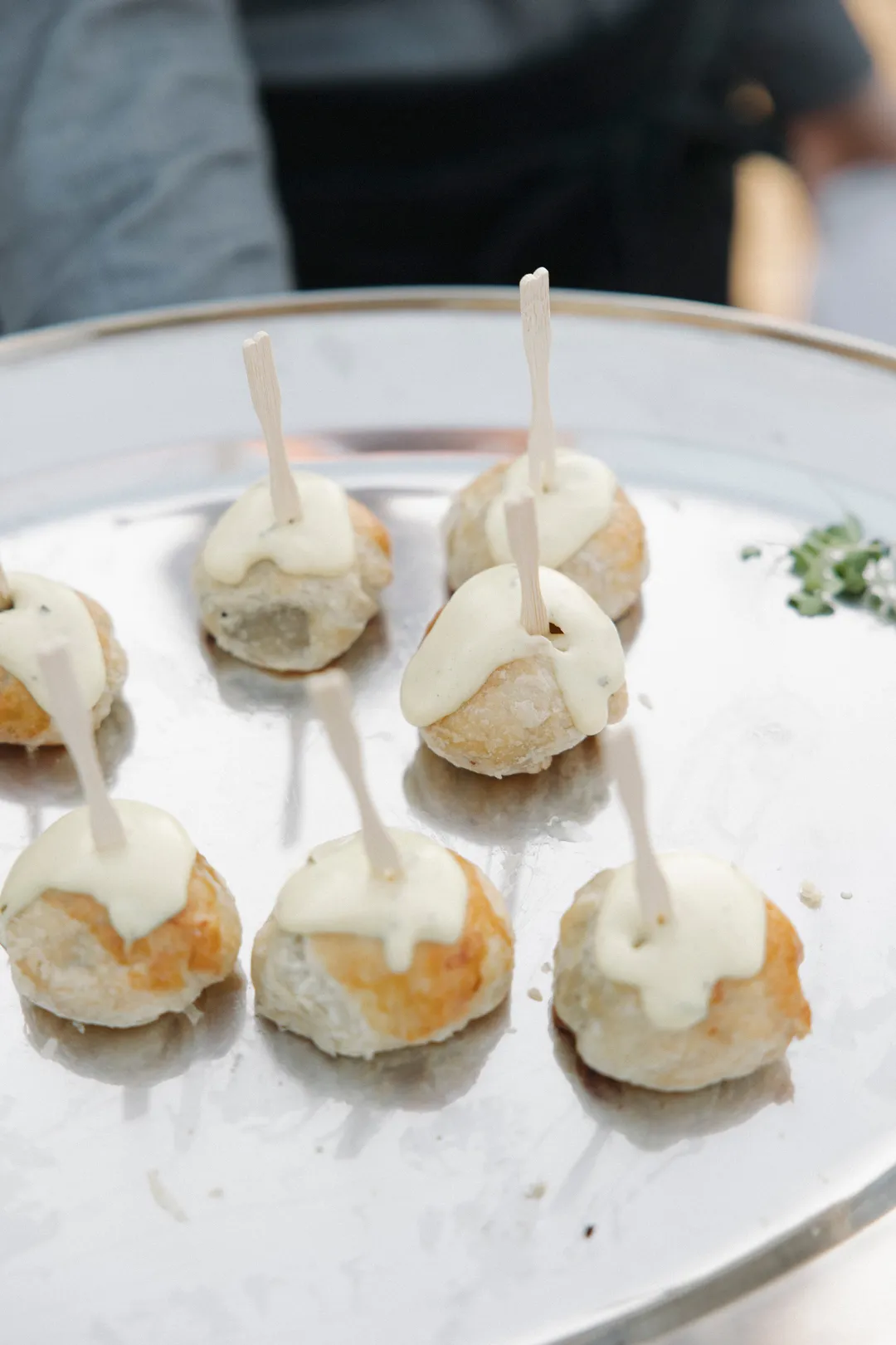 Golden bite-sized appetizers topped with sauce on a silver platter.