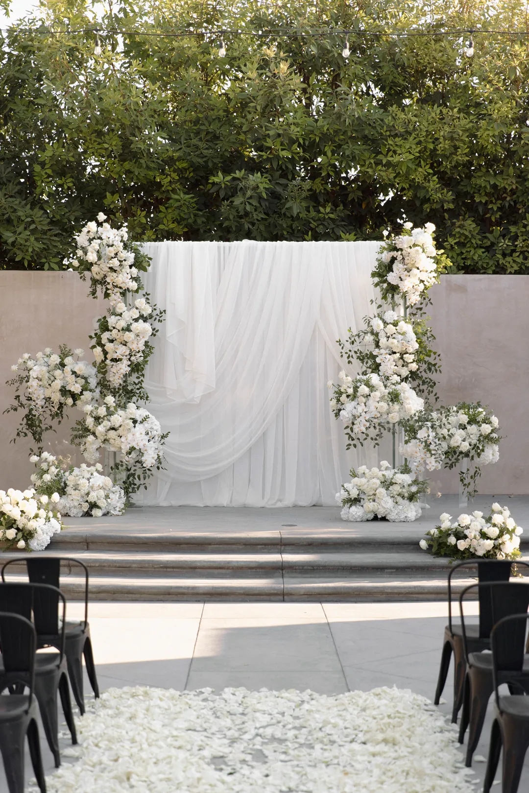White-draped ceremony backdrop framed by white flowers.