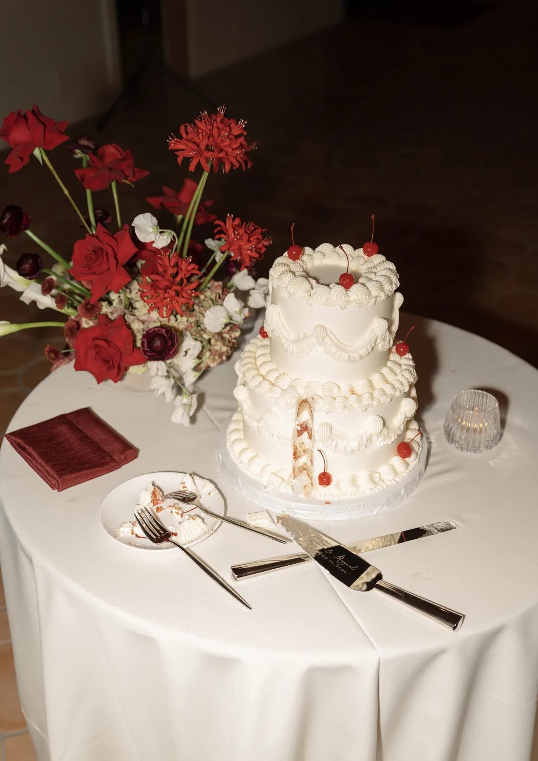 White piped wedding cake with red accents beside a floral arrangement.
