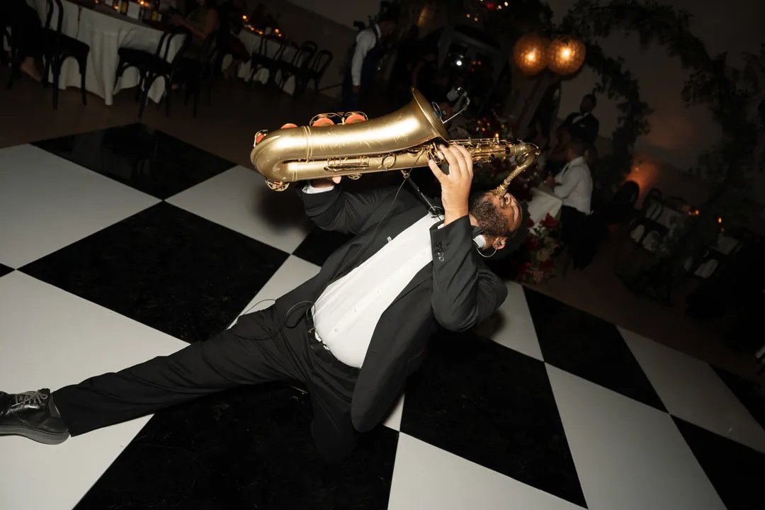 Saxophonist leaning back while performing on the checkered dance floor.