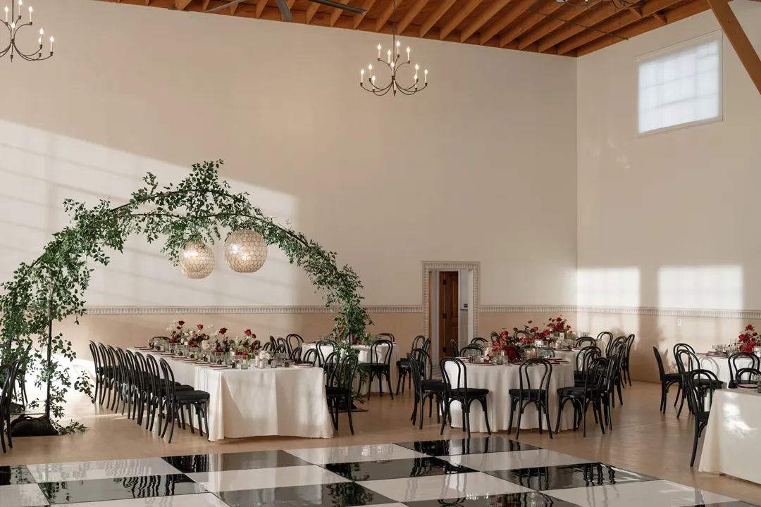 Greenery arch framing reception tables beside the checkered dance floor.