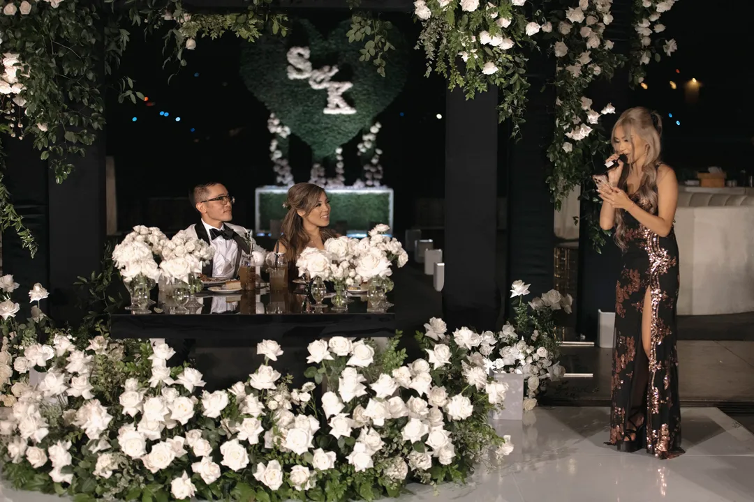 Guest giving a toast beside the couple's flower-framed sweetheart table.
