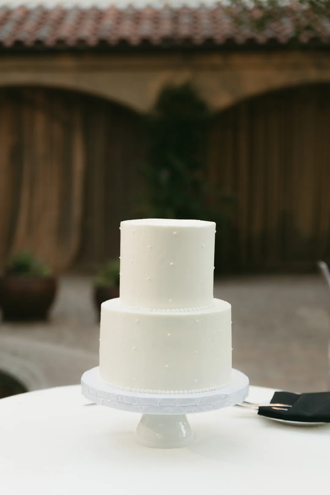 Simple two-tier white wedding cake on a pedestal.