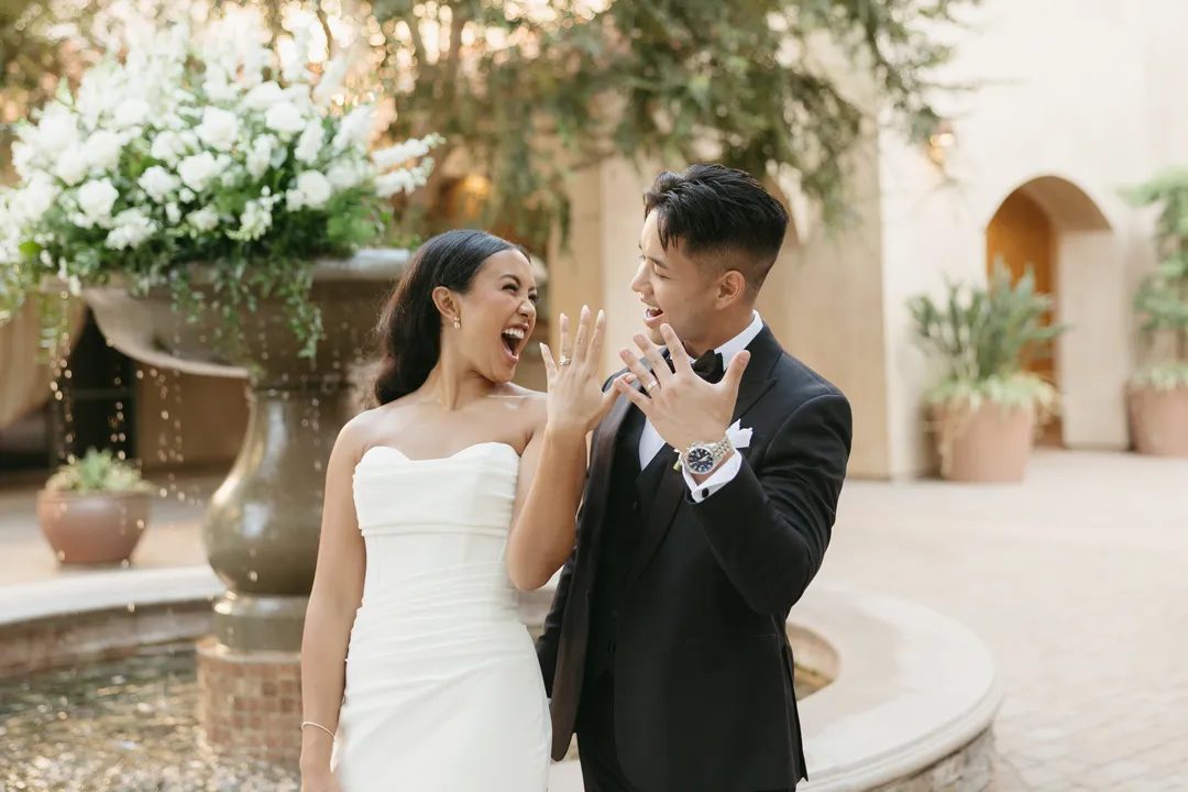Wedding couple smiling and showing their rings beside the fountain.