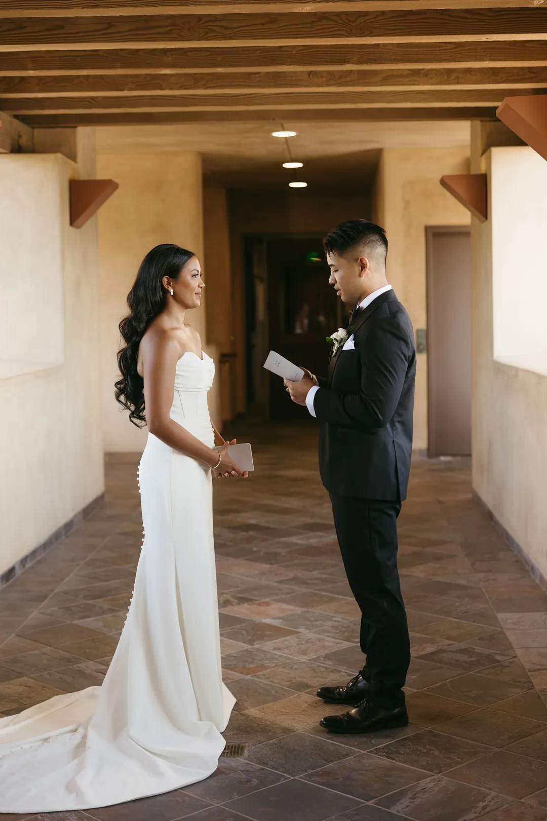 Groom reading a note to the bride beneath exposed wooden beams.