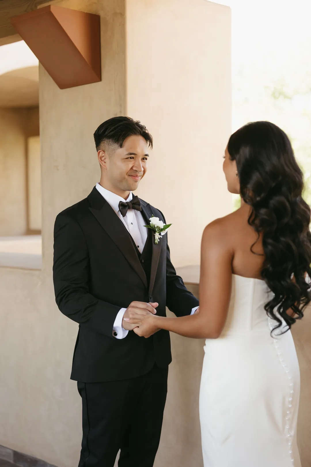 Wedding couple holding hands beneath a covered courtyard walkway.