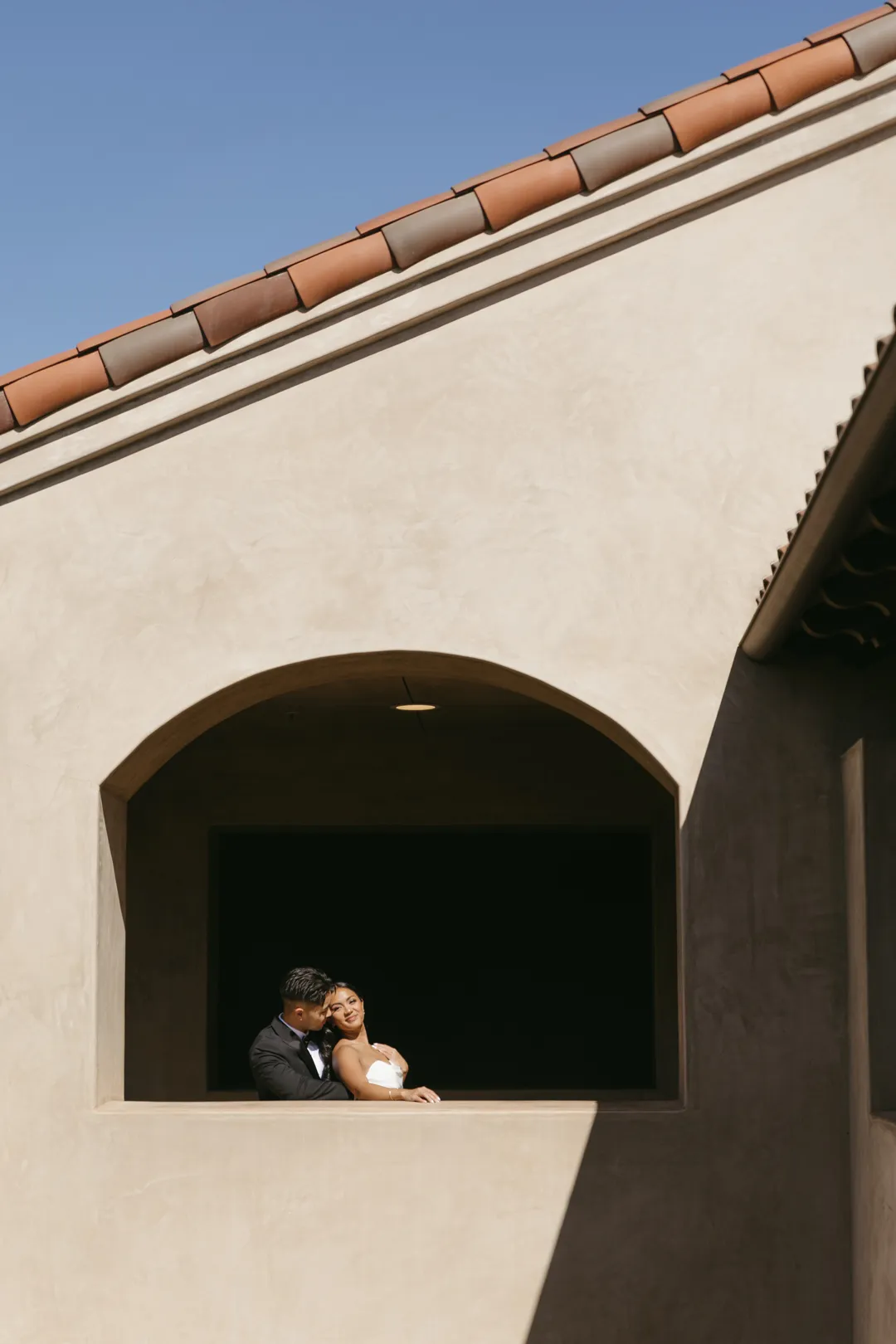 Wedding couple framed by an upper-level stucco opening.