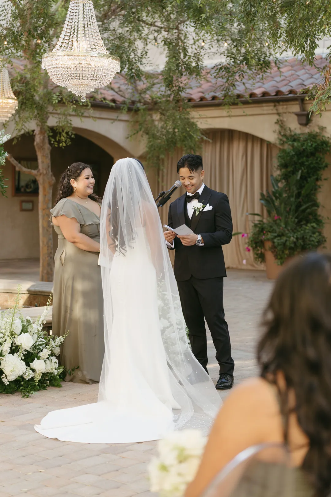 Wedding couple exchanging vows beneath a chandelier.