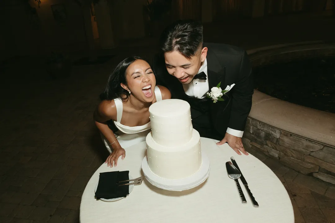 Wedding couple laughing beside their two-tier cake.