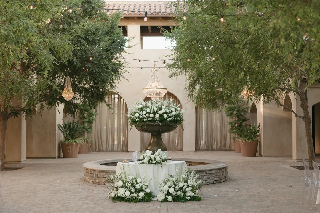 Courtyard fountain decorated with white flowers beneath chandeliers.