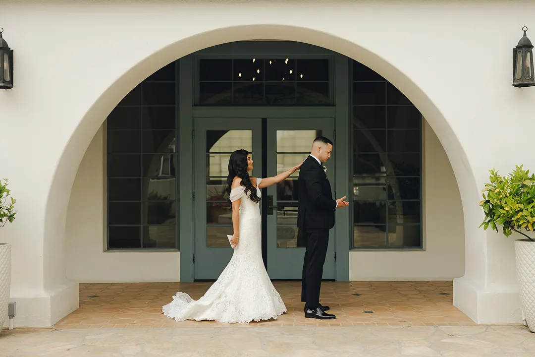 Bride approaching the groom for their first look beneath an archway.