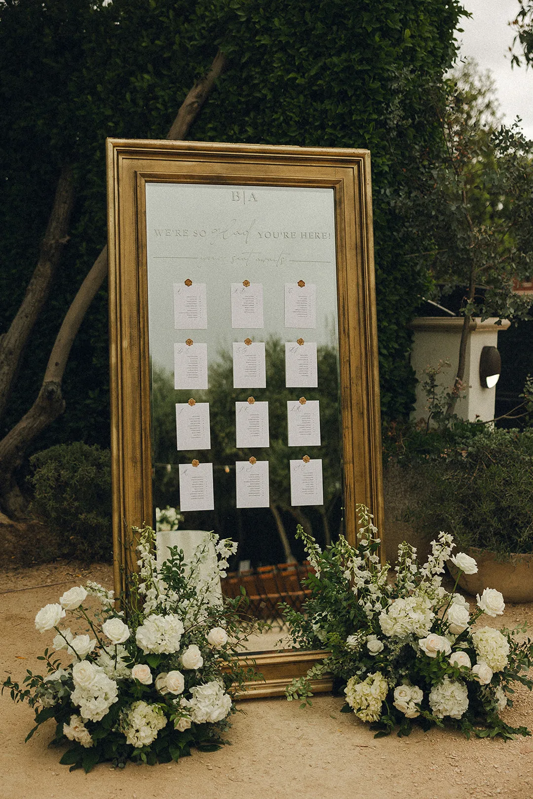 Gold-framed seating chart with white flowers at its base.