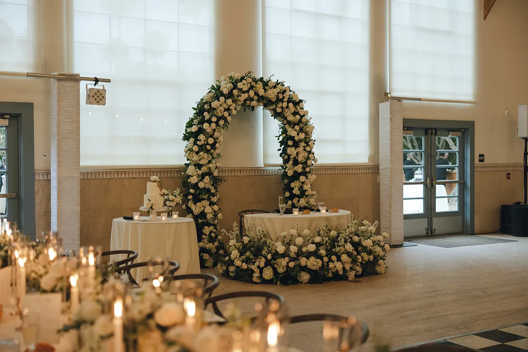 Sweetheart table framed by a white floral arch indoors.