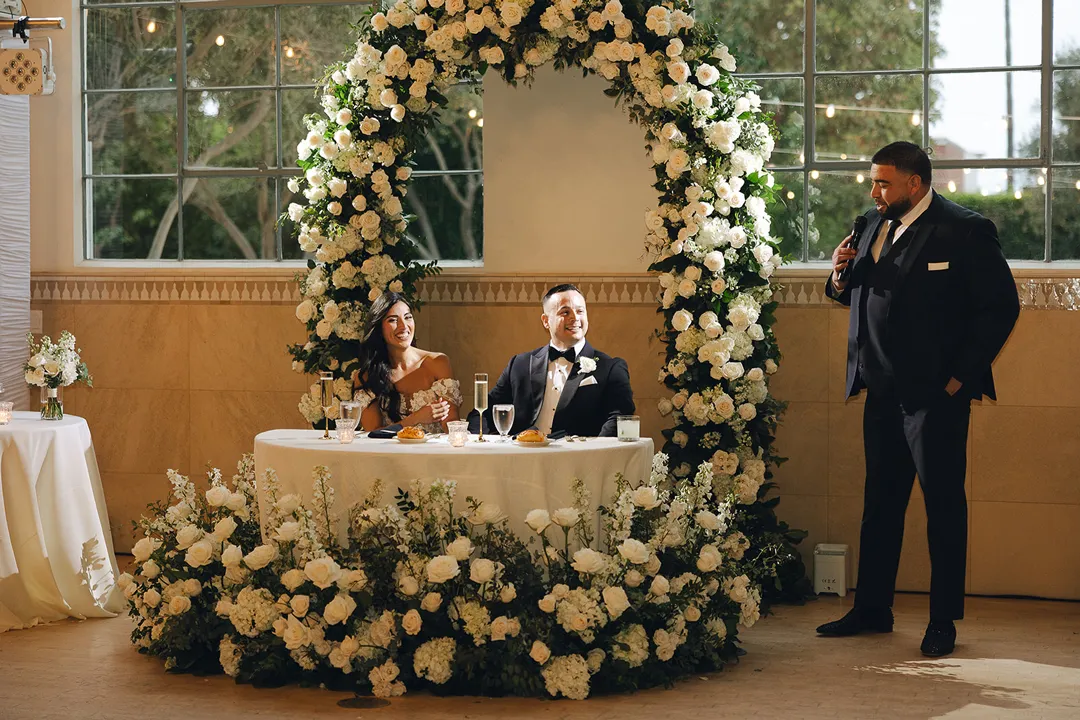 Guest giving a toast beside the couple's flower-framed table.