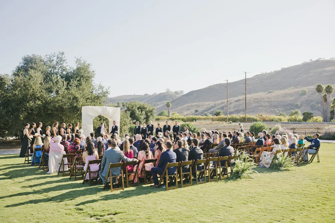 Guests seated for an outdoor ceremony with hills in the background.