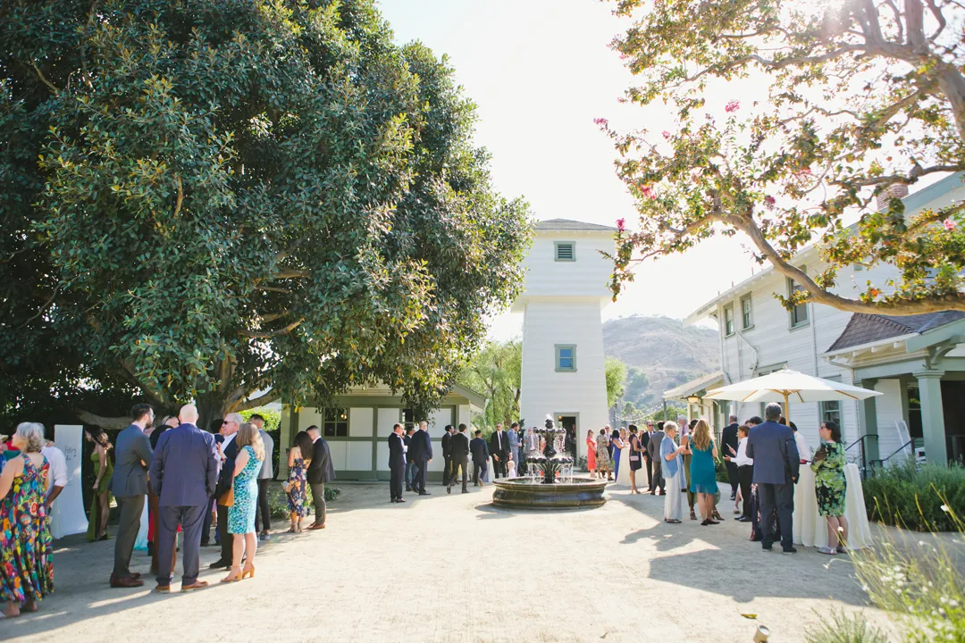 Wedding guests mingling outside the pale-yellow house.