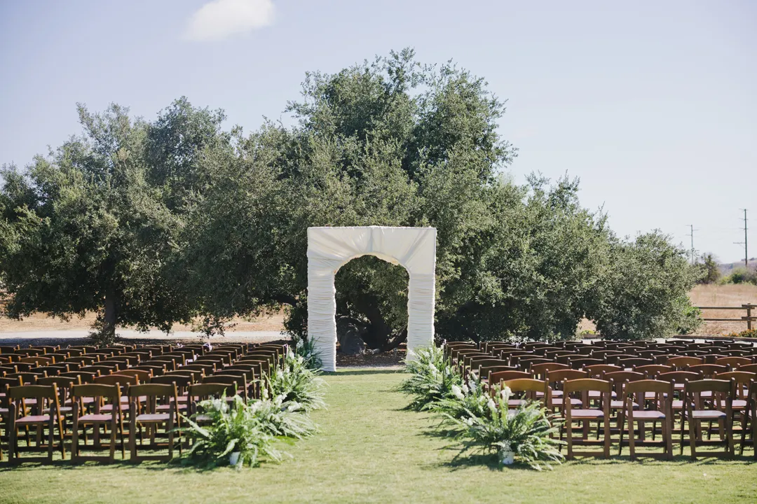 Lawn ceremony aisle with ferns and a white fabric-covered arch.
