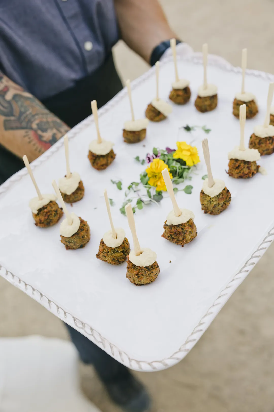 Server carrying a tray of bite-sized appetizers with sauce.
