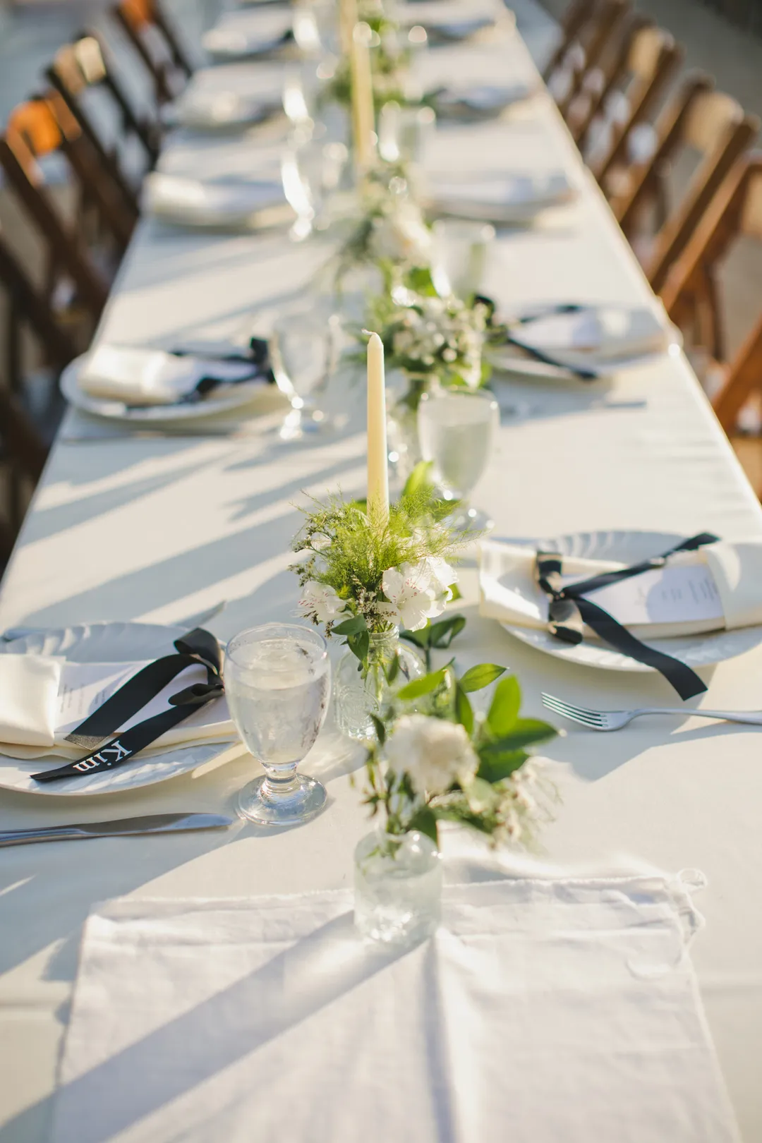Long reception table with white linens, greenery and taper candles.