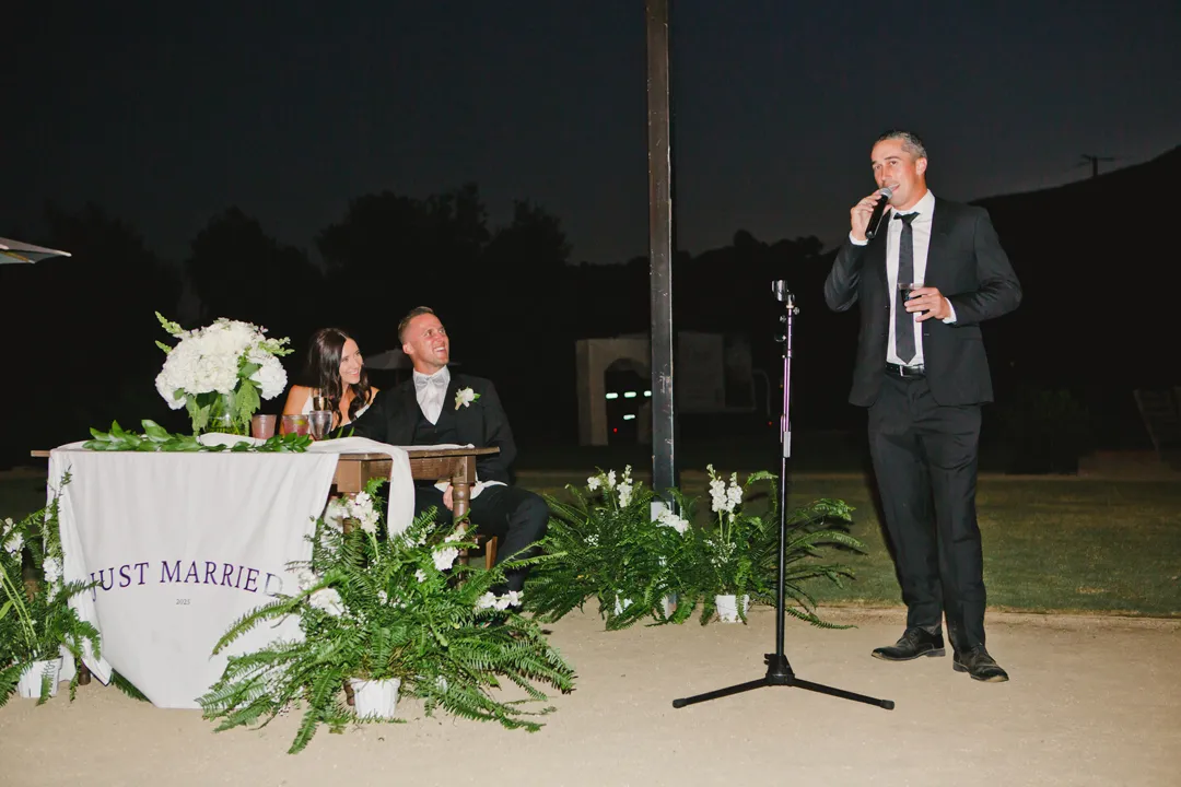 Guest giving a toast beside the couple's greenery-decorated table.