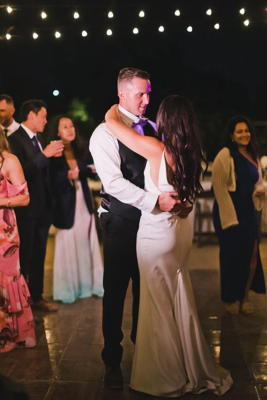 Wedding couple dancing together under strings of lights at night.