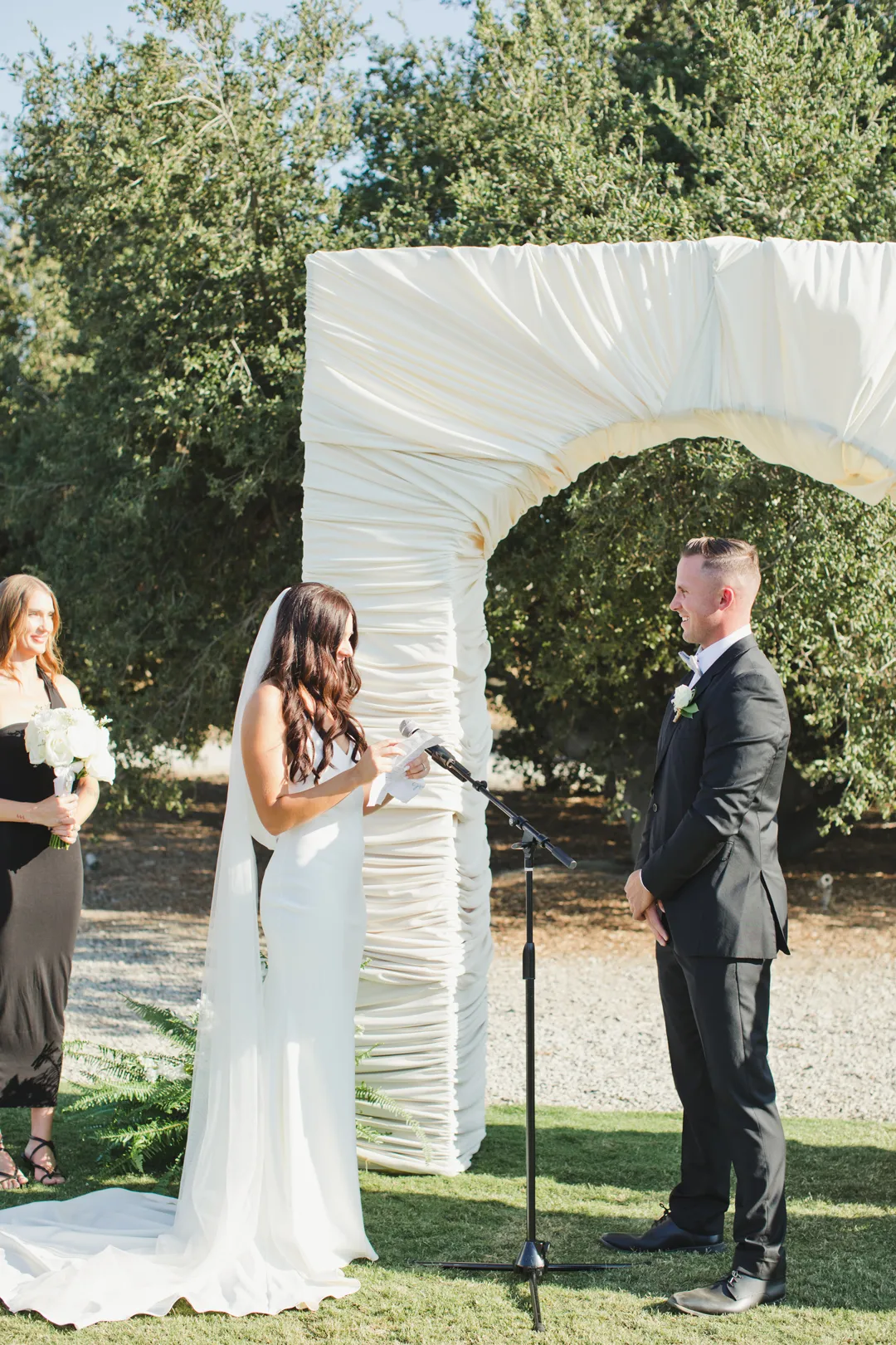 Bride reading her vows beside the white ceremony arch.