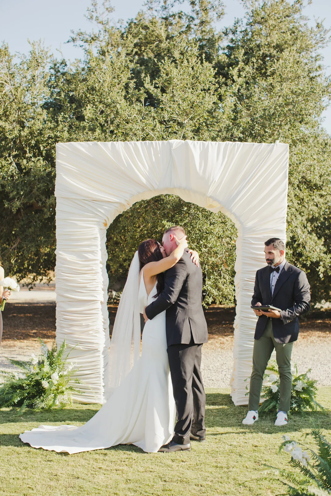 Wedding couple kissing beneath the white fabric-covered arch.
