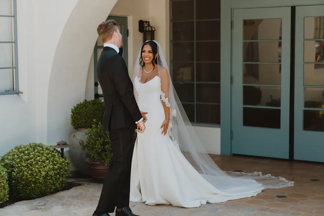Wedding couple smiling beneath an arch beside green doors.