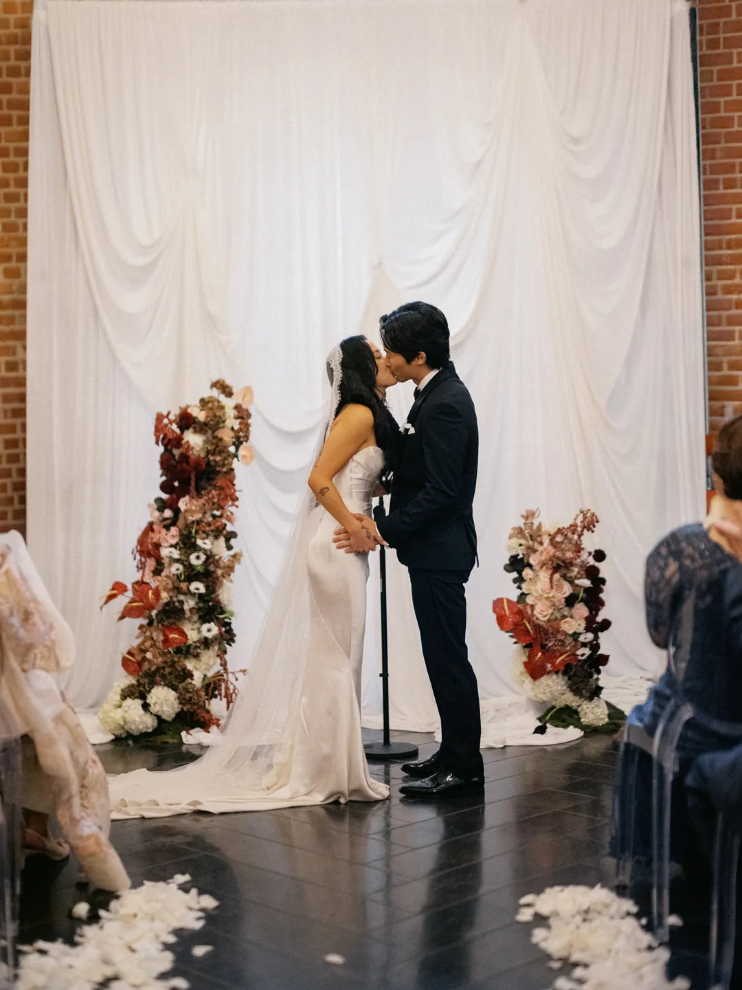 Wedding couple kissing in front of the draped ceremony backdrop.