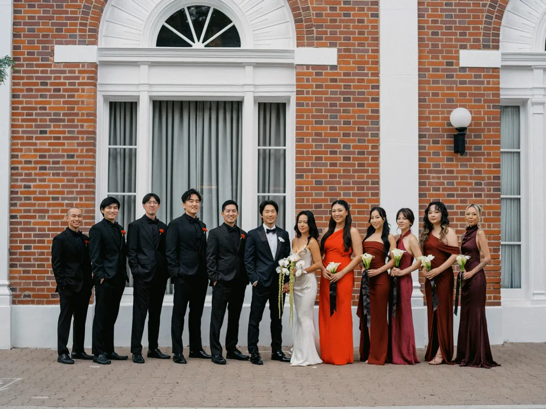 Wedding party posing against the red-brick facade.