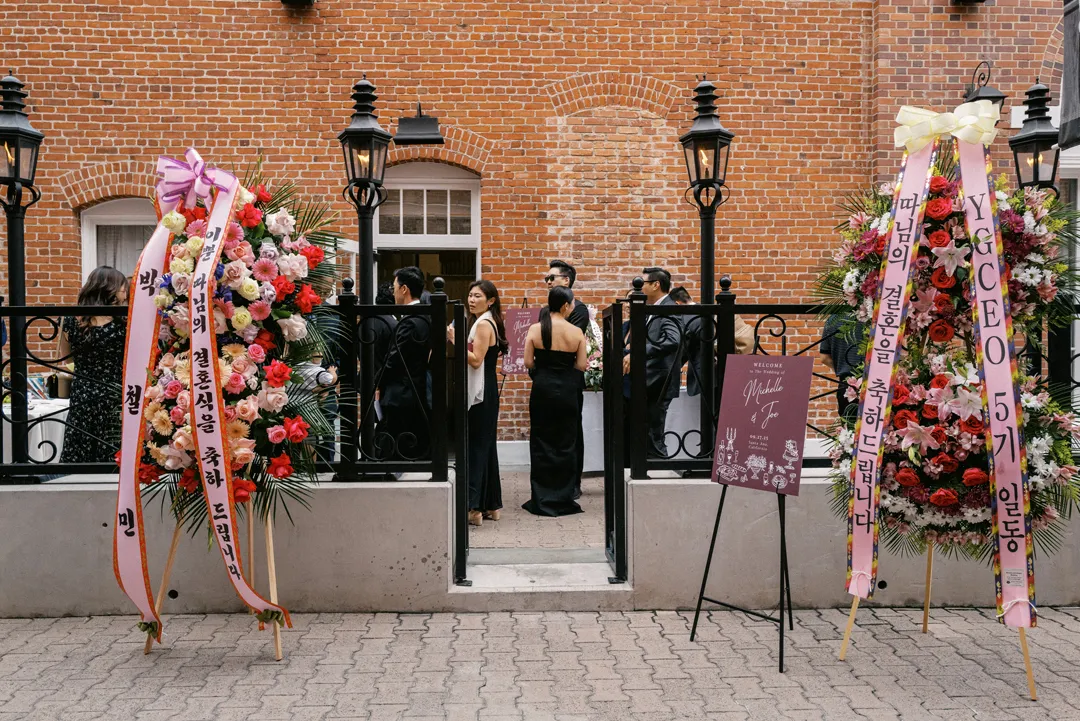 Guests entering between tall floral arrangements at the courtyard gate.