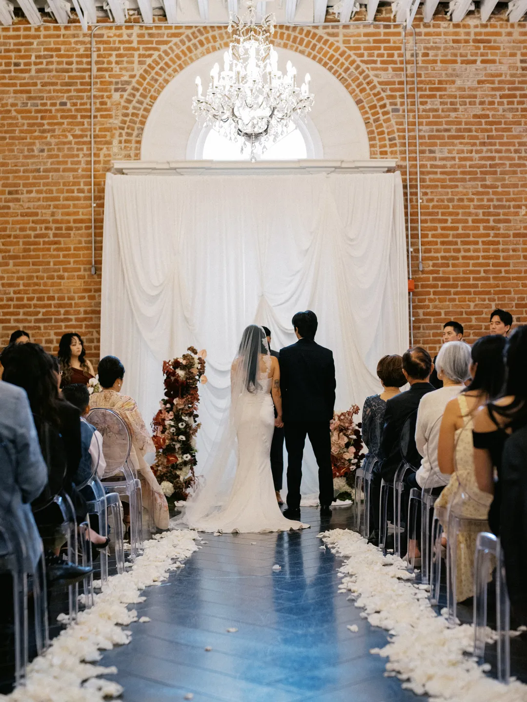 Wedding guests watching the ceremony along a petal-lined aisle.