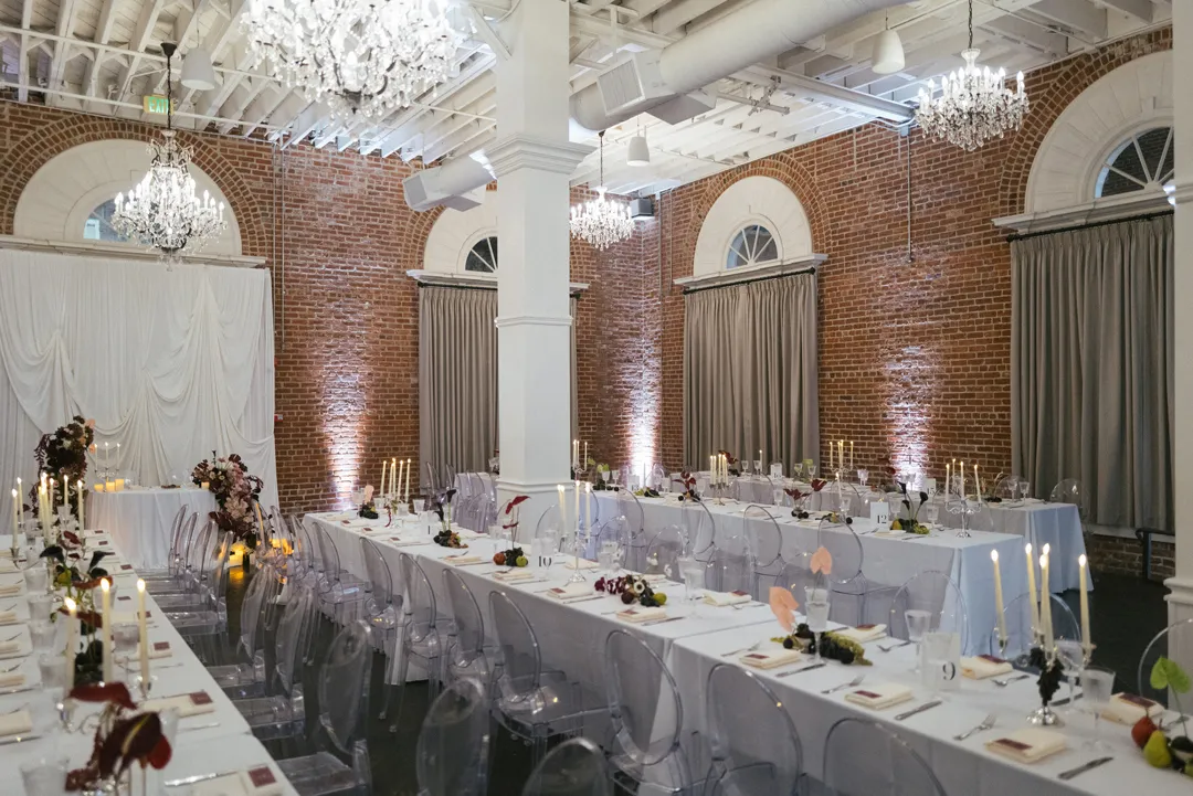Brick reception hall with chandeliers and white-linen tables.