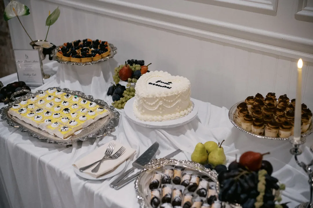 Wedding cake, miniature desserts and fruit on a draped table.