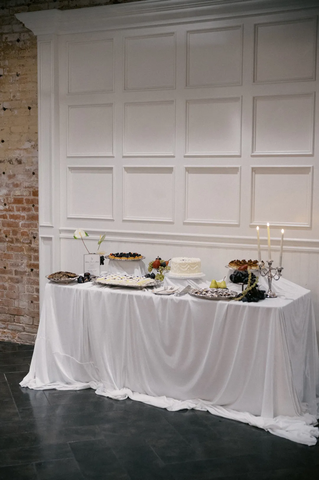 White-draped dessert table beneath a paneled wall.