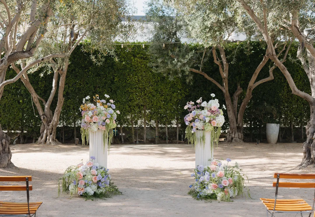 Pastel floral arrangements on white columns beneath olive trees.