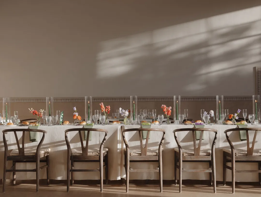 Long reception table with small floral arrangements in warm sunlight.