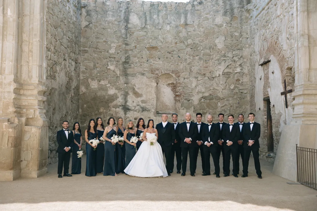 Wedding party posing between historic stone walls.