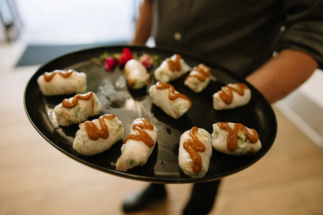 Server presenting bite-sized appetizers topped with sauce.