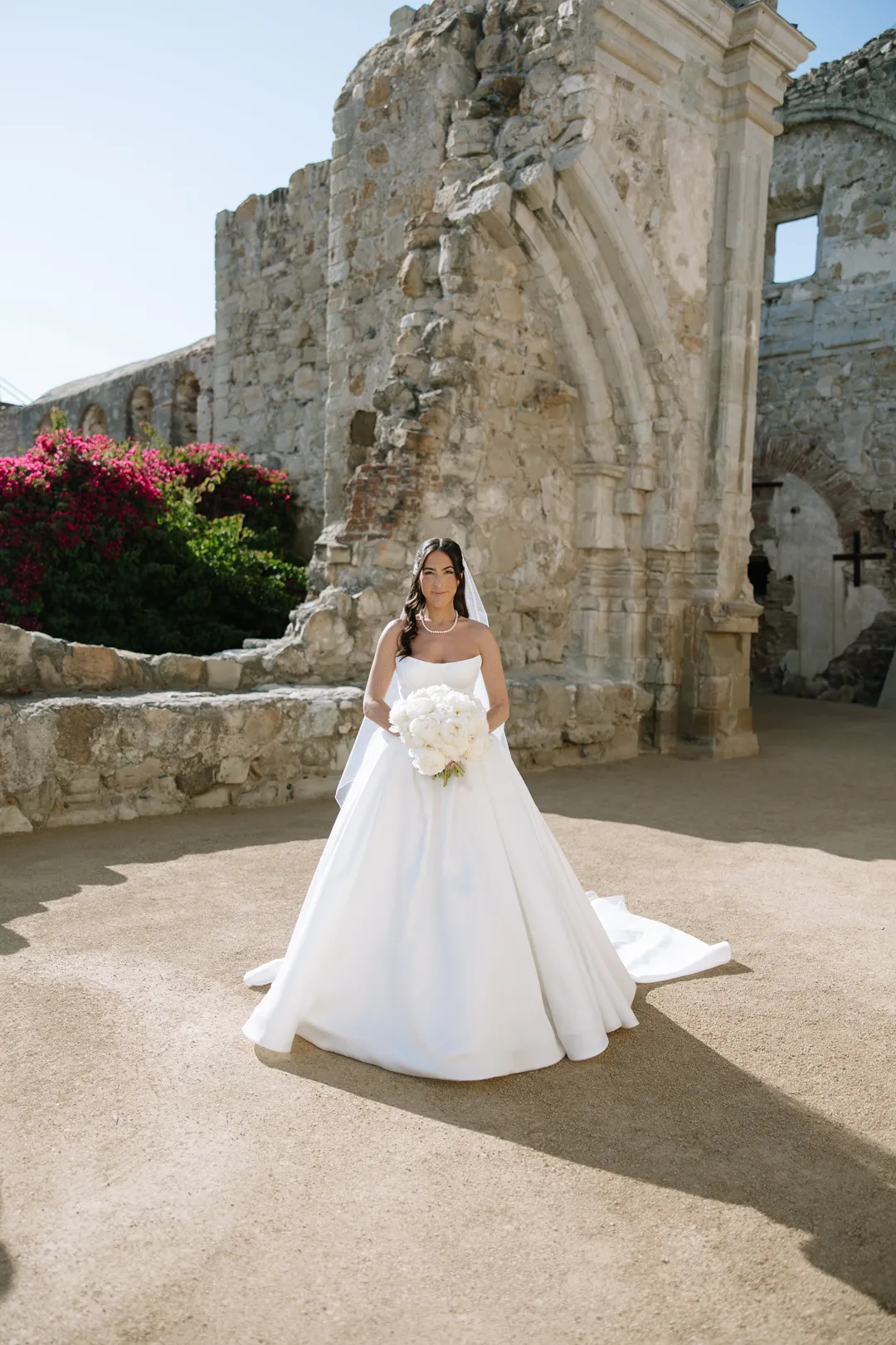 Bride posing with her bouquet beside stone ruins.