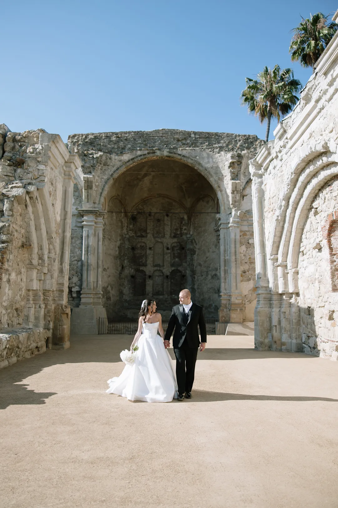Wedding couple walking together through a historic stone courtyard.